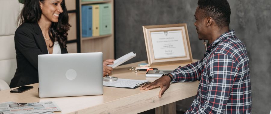 Une conseillère présente un document à un client assis en face d'elle, ordinateur ouvert sur le bureau