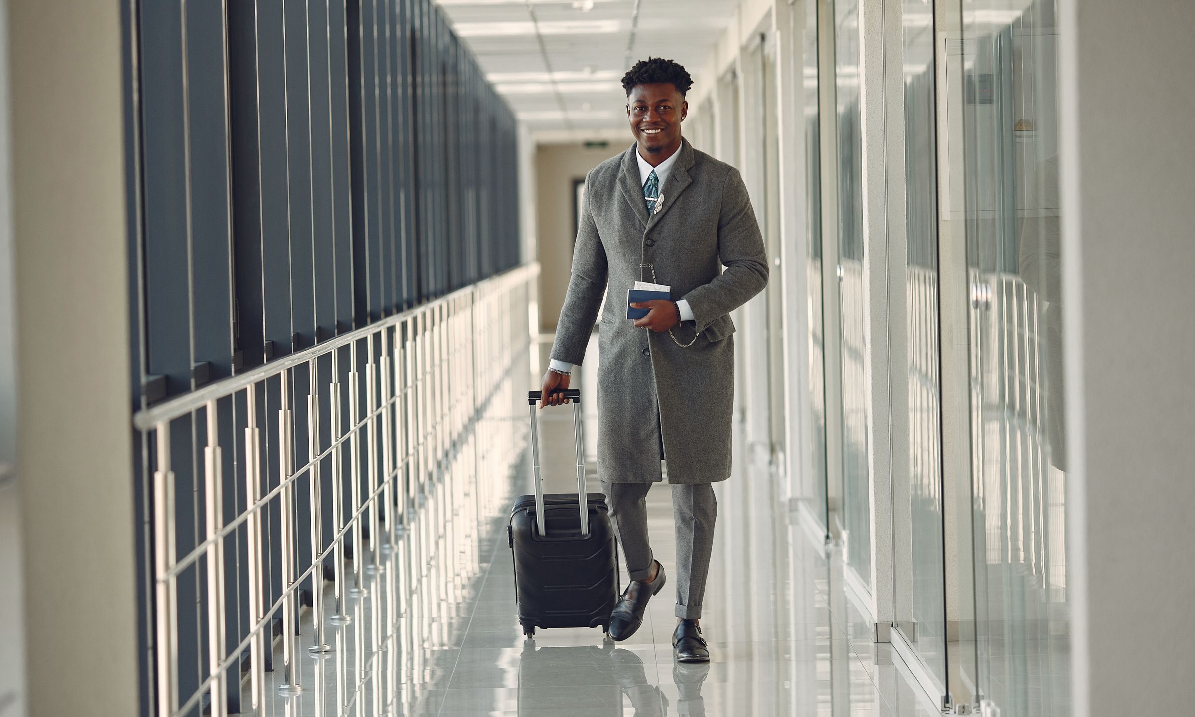 Un homme souriant traverse le couloir d'un aéroport, passeport à la main, en tirant sa valise