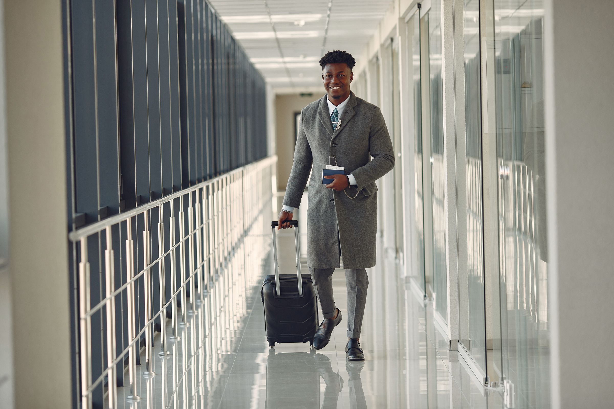 Un homme souriant traverse le couloir d'un aéroport, passeport à la main, en tirant sa valise