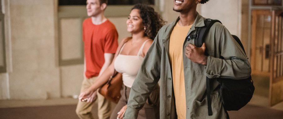 Trois étudiants marchent ensemble dans un couloir de campus, sac à dos sur l'épaule
